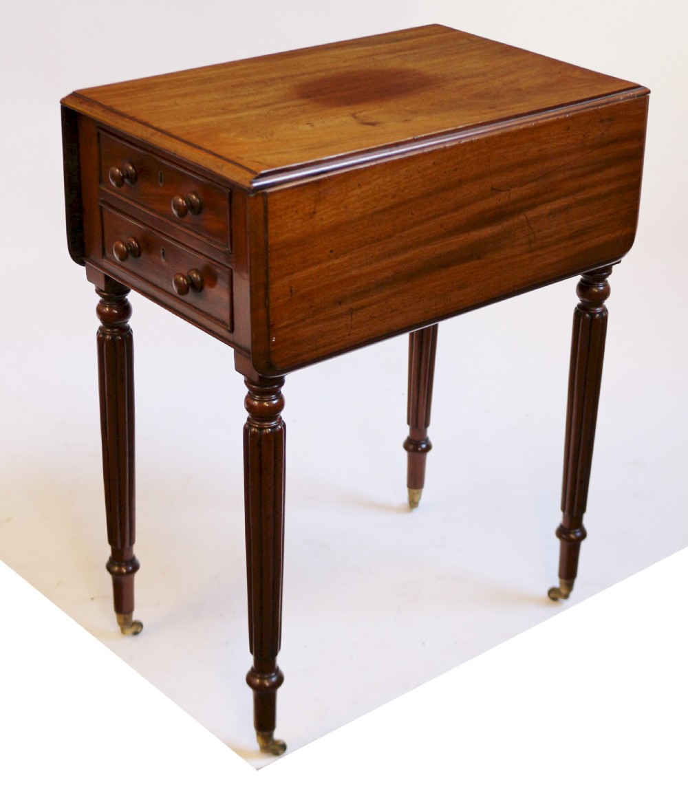 A William IV mahogany drop-leaf table featuring two drawers with wooden knobs, reeded legs, and brass castors. View IV