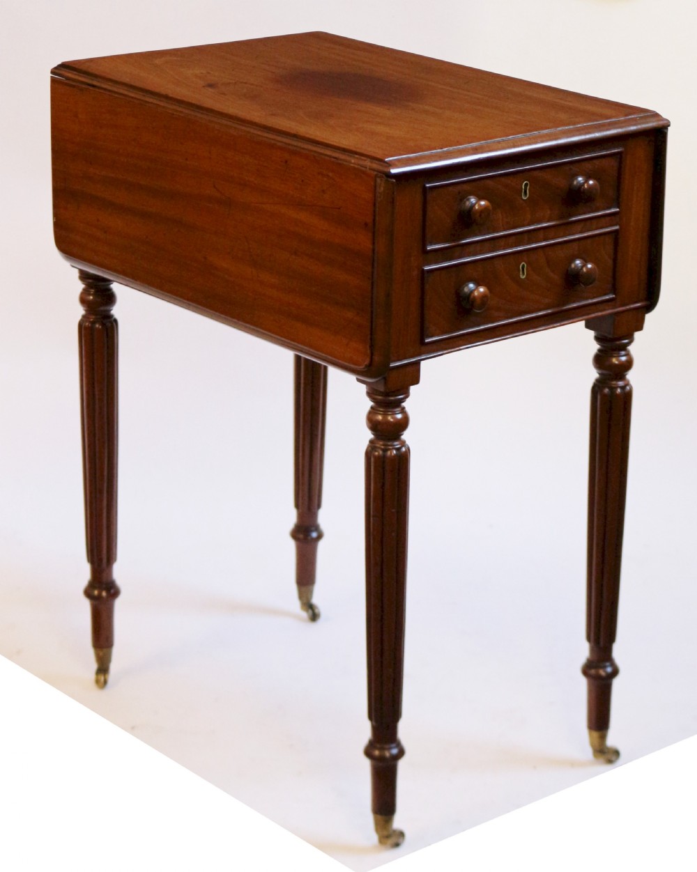 A William IV mahogany drop-leaf table featuring two drawers with wooden knobs, reeded legs, and brass castors. View V