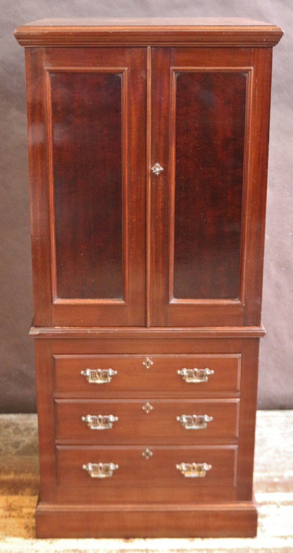 An Edwardian mahogany safe cabinet featuring twin upper panelled doors over three drawers with brass drop handles on a plinth base.