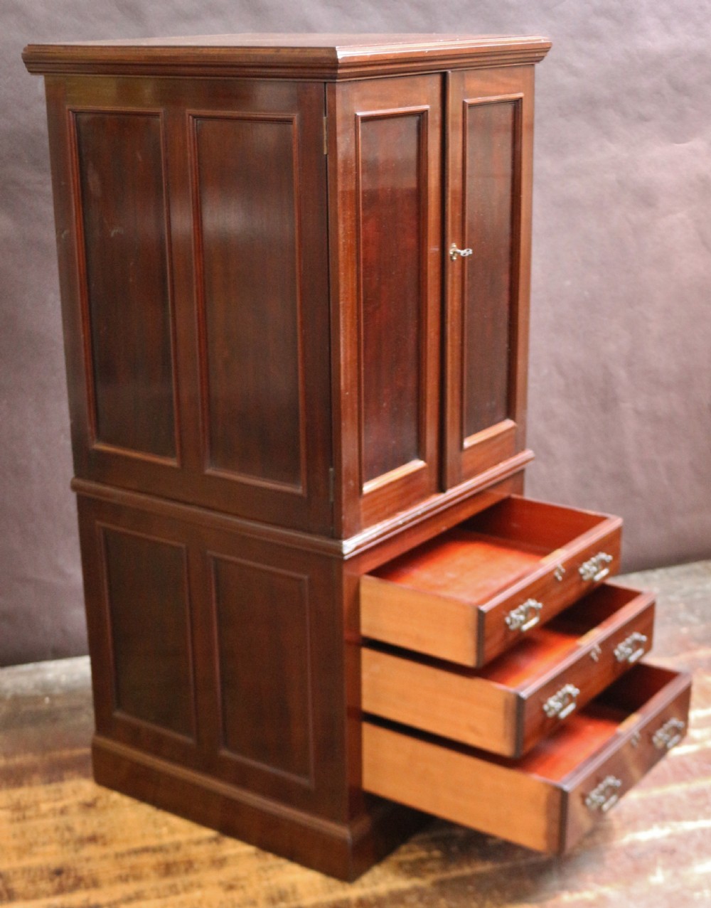 An Edwardian mahogany safe cabinet featuring twin upper panelled doors over three drawers with brass drop handles on a plinth base. View III