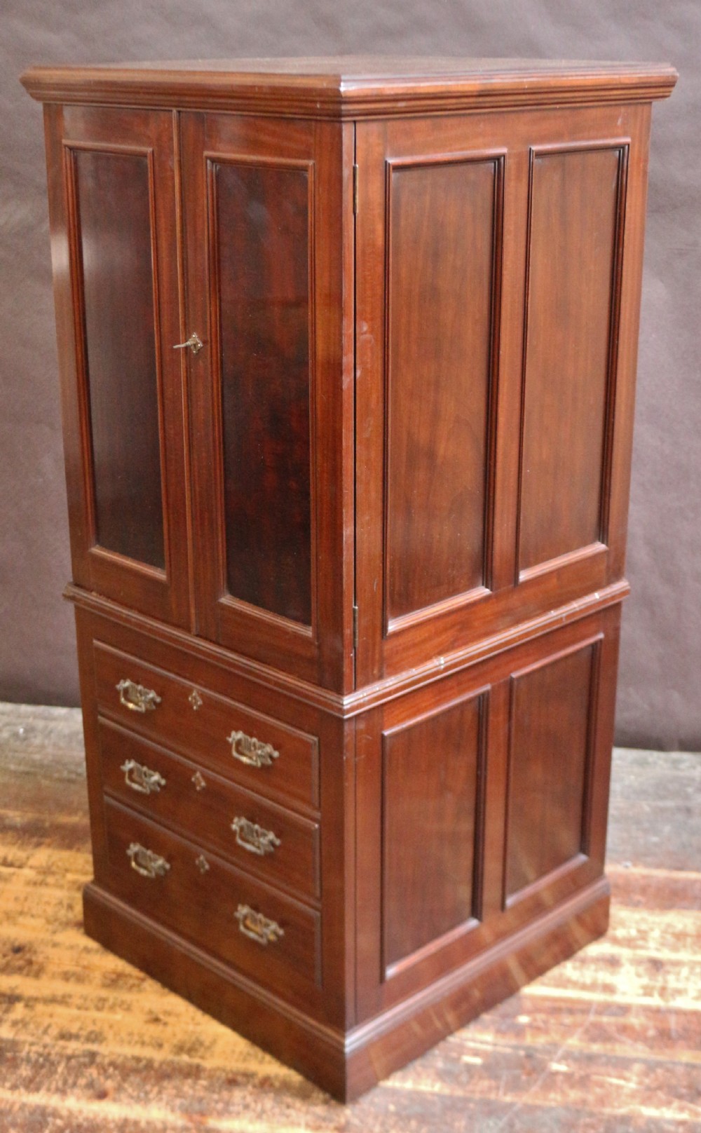 An Edwardian mahogany safe cabinet featuring twin upper panelled doors over three drawers with brass drop handles on a plinth base. View VI
