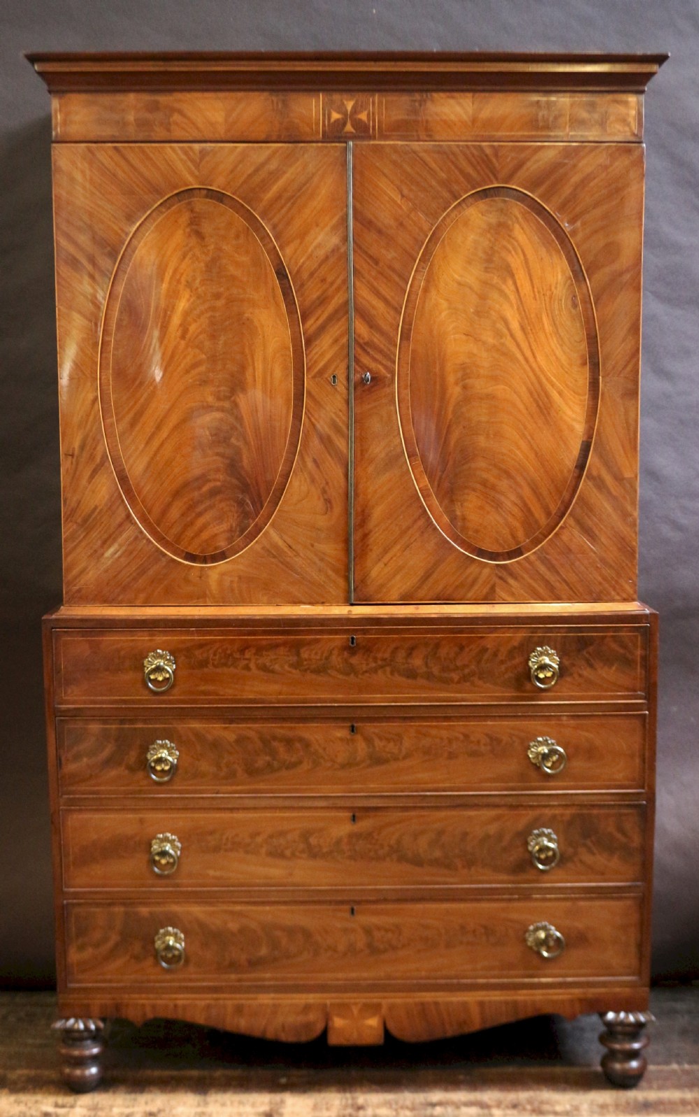 A George III mahogany linen press featuring oval flame mahogany veneered door panels above four drawers with brass handles.