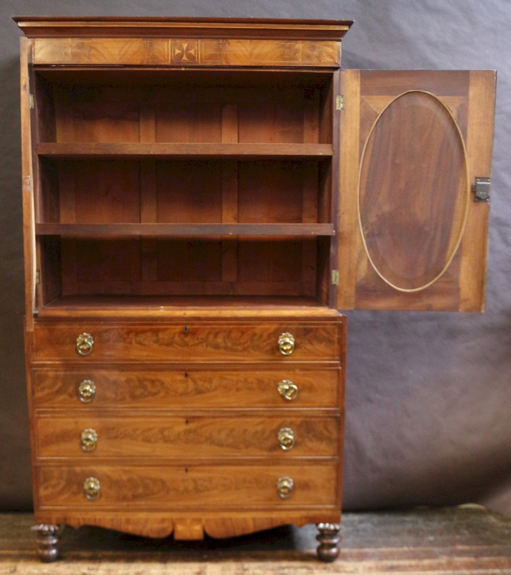 A George III mahogany linen press featuring oval flame mahogany veneered door panels above four drawers with brass handles. View II