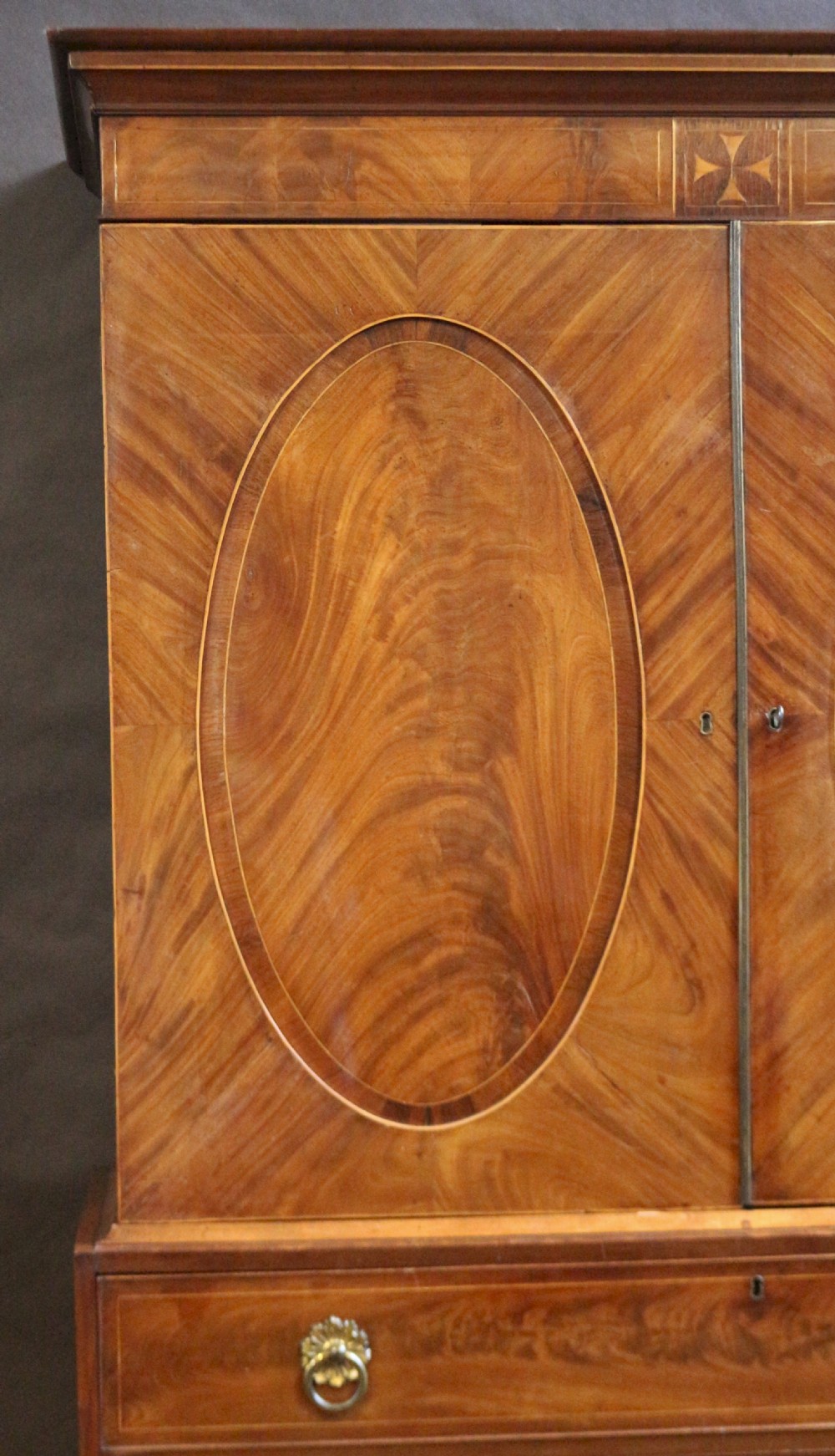 A George III mahogany linen press featuring oval flame mahogany veneered door panels above four drawers with brass handles. View III
