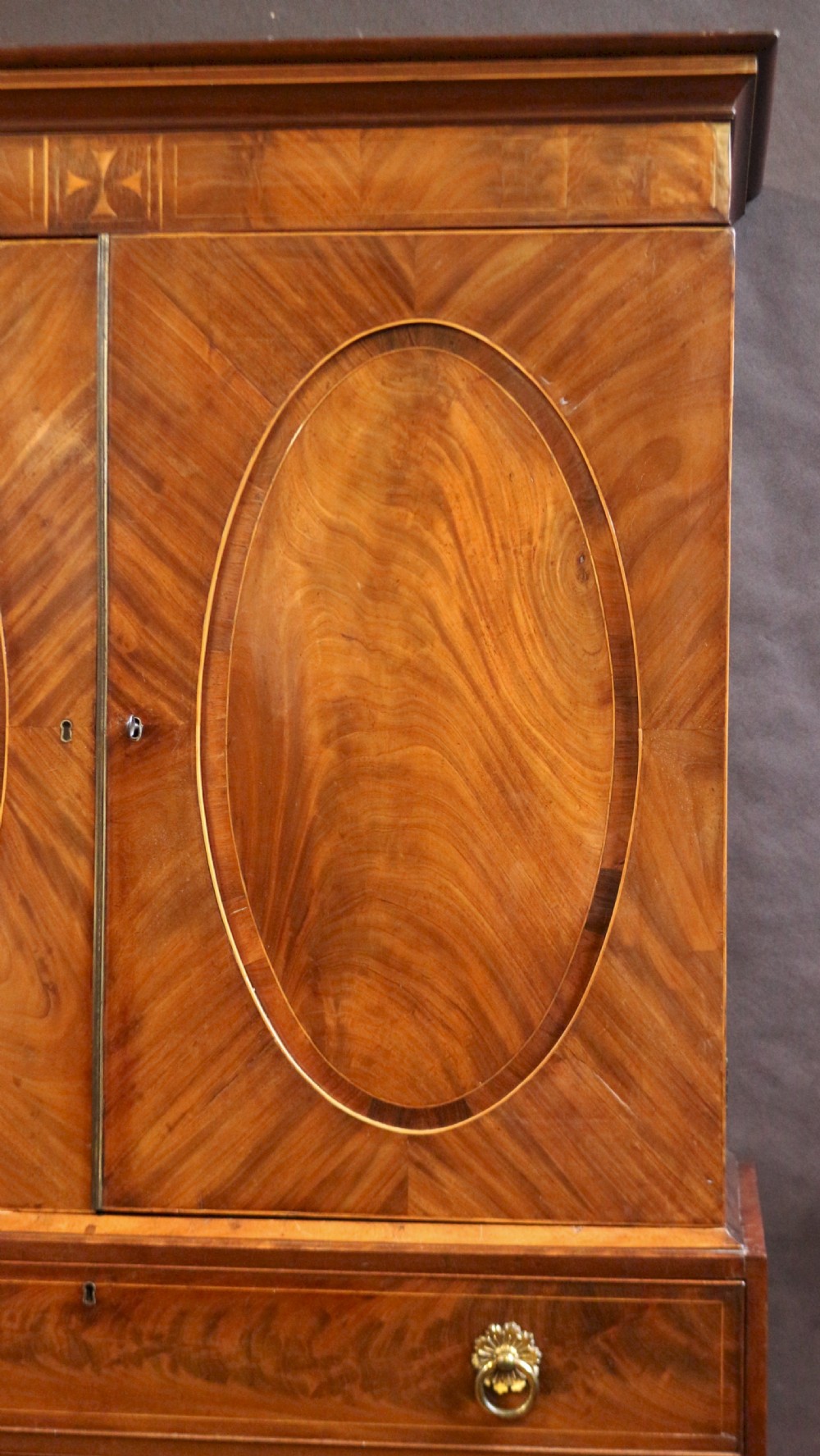 A George III mahogany linen press featuring oval flame mahogany veneered door panels above four drawers with brass handles. View IV