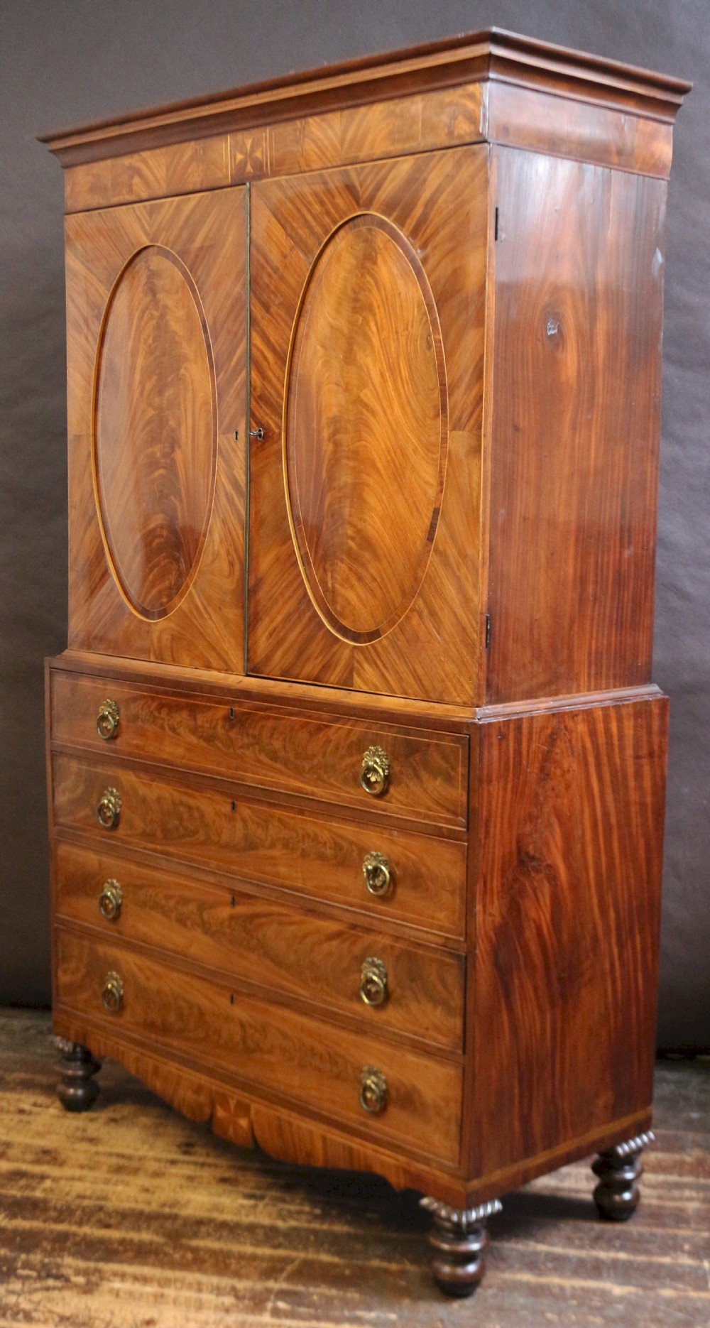 A George III mahogany linen press featuring oval flame mahogany veneered door panels above four drawers with brass handles. View VII