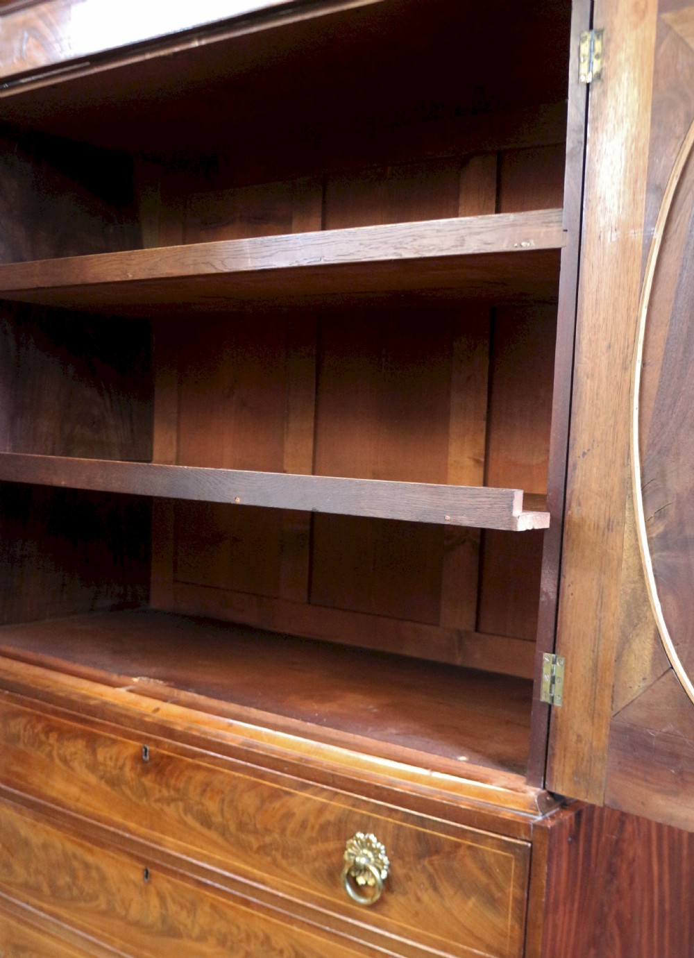 A George III mahogany linen press featuring oval flame mahogany veneered door panels above four drawers with brass handles. View XI