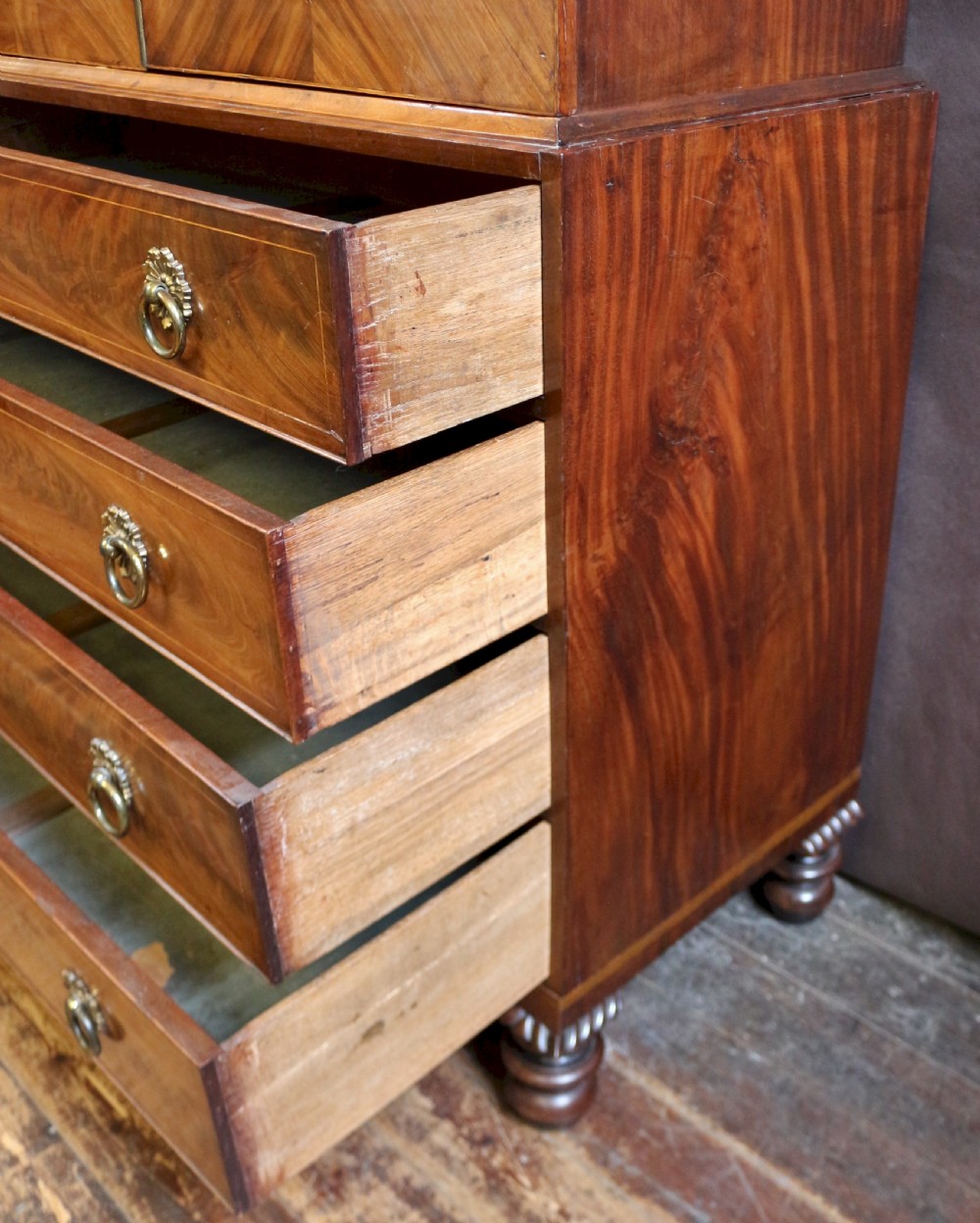 A George III mahogany linen press featuring oval flame mahogany veneered door panels above four drawers with brass handles. View XII