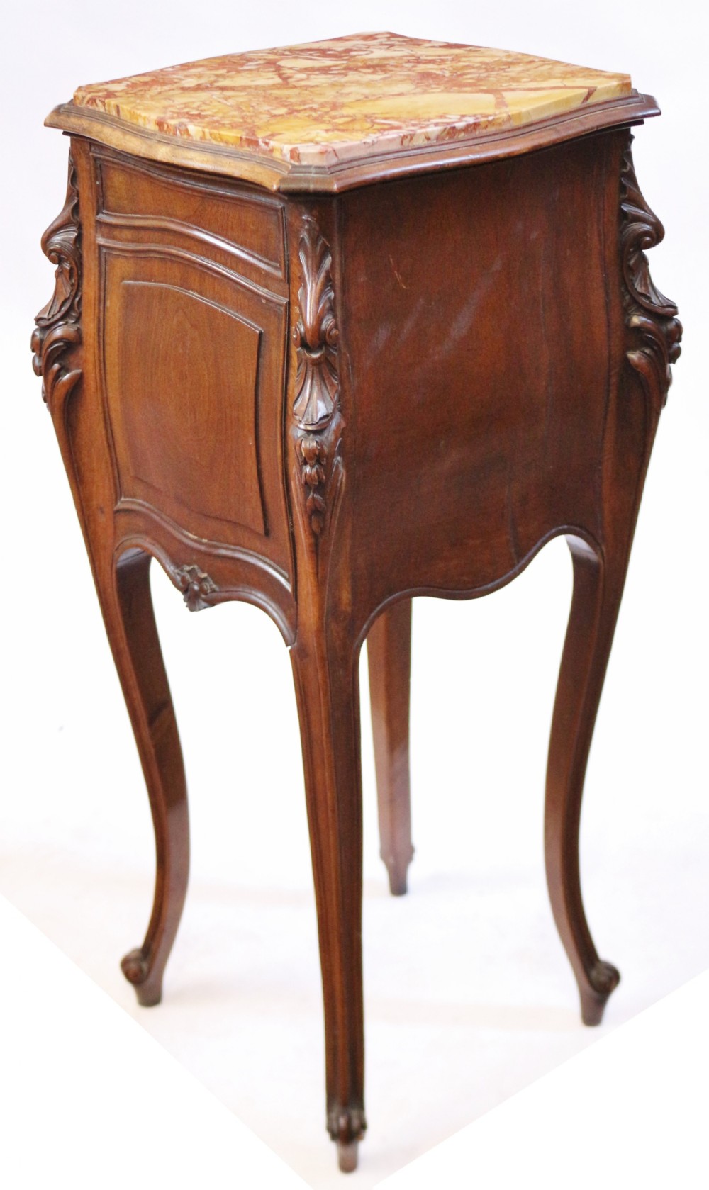 A 19th-century French walnut bedside cupboard featuring an inset variegated marble top, a top drawer, a quarter-veneered cupboard door, ornate rocaille carvings, and slender cabriole legs. View V
