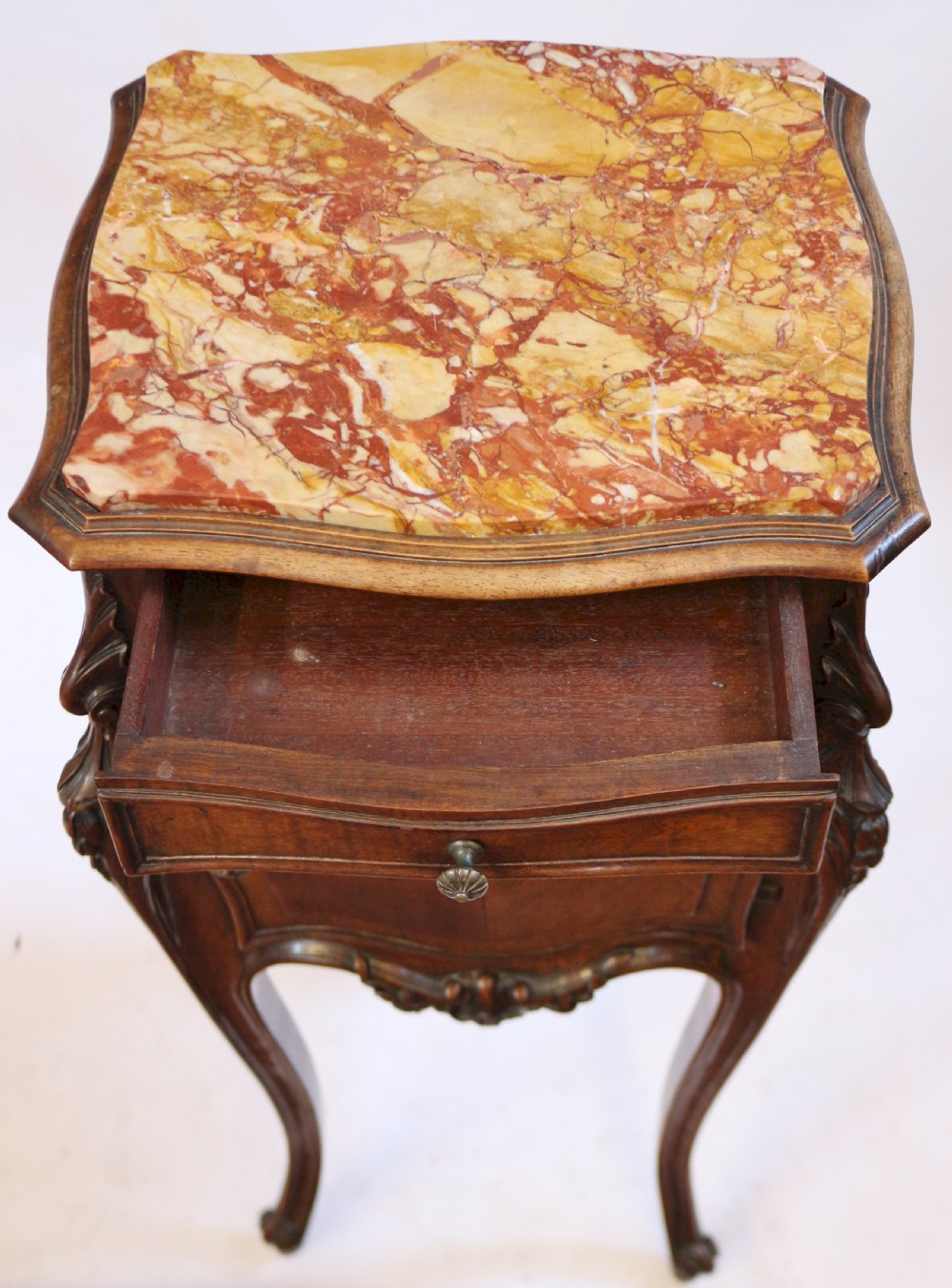 A 19th-century French walnut bedside cupboard featuring an inset variegated marble top, a top drawer, a quarter-veneered cupboard door, ornate rocaille carvings, and slender cabriole legs. View VII