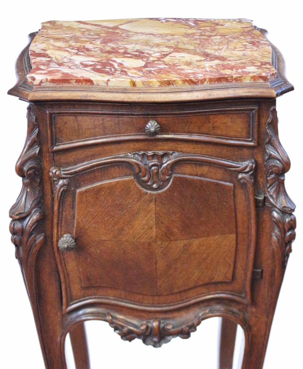 A 19th-century French walnut bedside cupboard featuring an inset variegated marble top, a top drawer, a quarter-veneered cupboard door, ornate rocaille carvings, and slender cabriole legs. View VIII