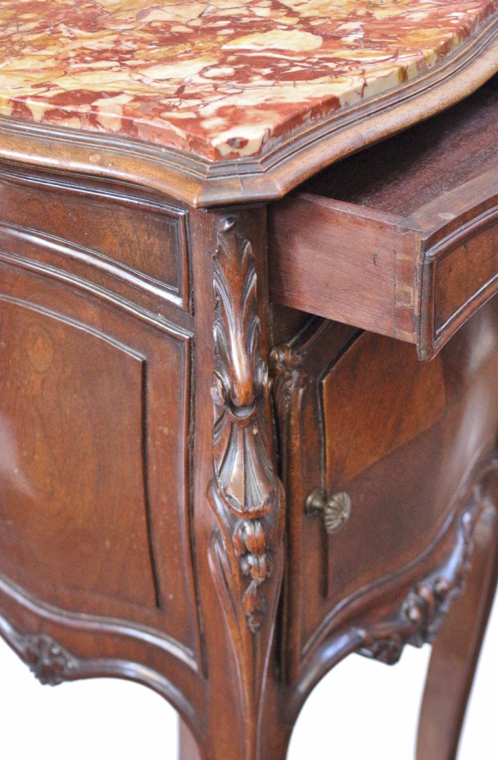 A 19th-century French walnut bedside cupboard featuring an inset variegated marble top, a top drawer, a quarter-veneered cupboard door, ornate rocaille carvings, and slender cabriole legs. View IX