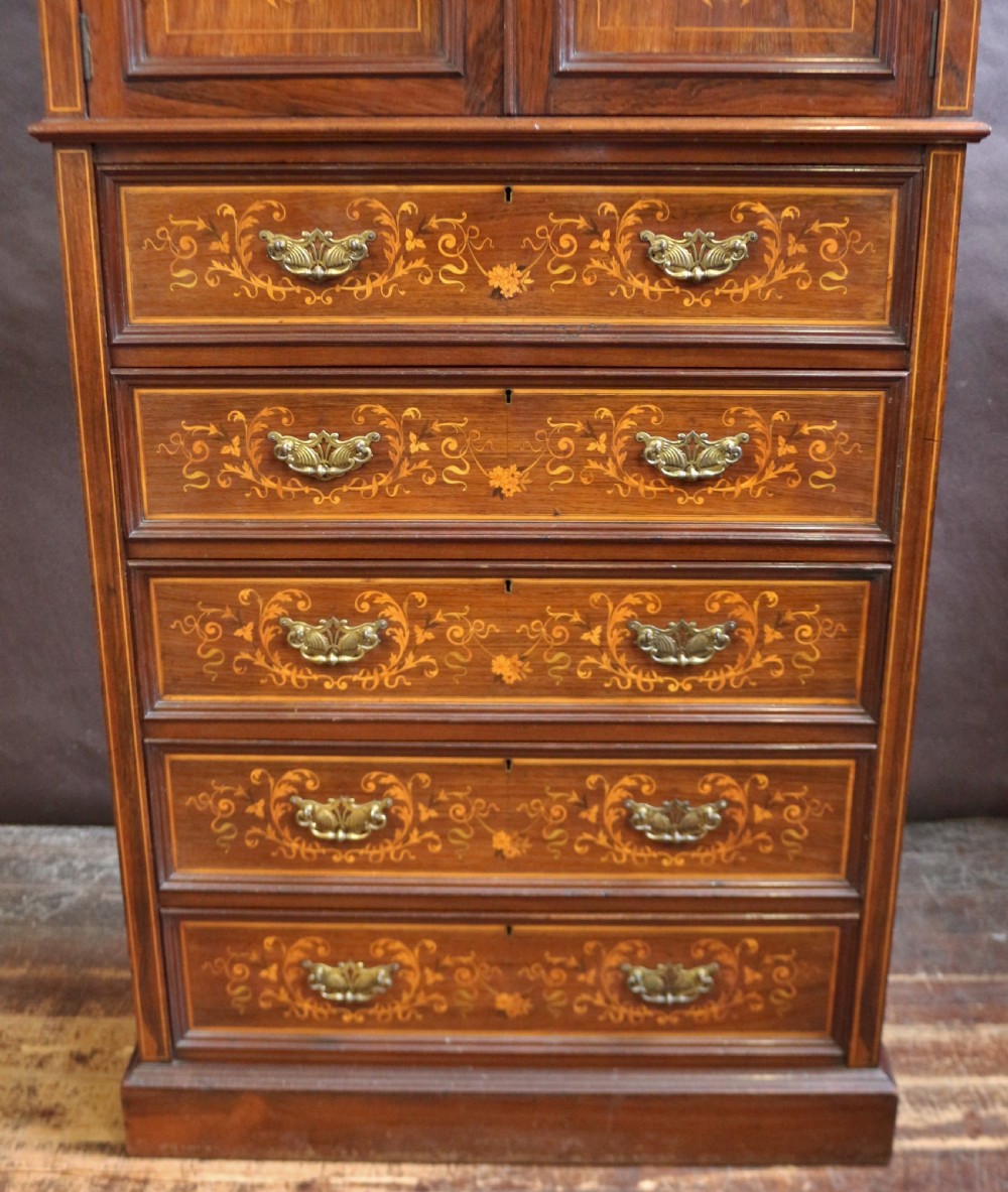 An Edwardian rosewood cupboard on chest featuring elaborate floral satinwood marquetry inlay, a two-door upper section, and five lower drawers with brass handles. View VI