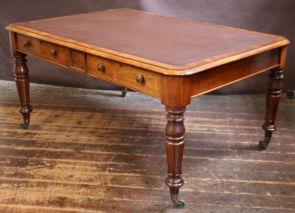 An early Victorian writing table in figured walnut featuring an inset brown leather top, four drawers with turned wooden knobs, and turned legs fitted with brass castors. View III