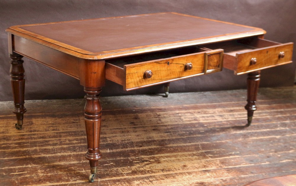 An early Victorian writing table in figured walnut featuring an inset brown leather top, four drawers with turned wooden knobs, and turned legs fitted with brass castors. View IV