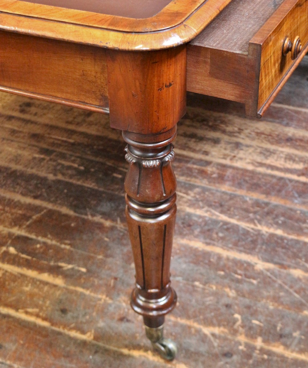 An early Victorian writing table in figured walnut featuring an inset brown leather top, four drawers with turned wooden knobs, and turned legs fitted with brass castors. View VII