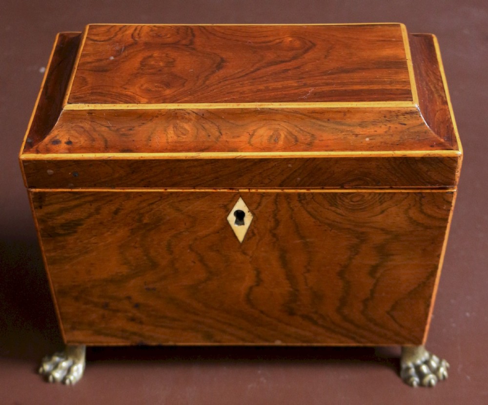 A Regency rosewood tapered oblong tea caddy featuring inlay stringing, a diamond bone escutcheon, and brass lion paw feet.