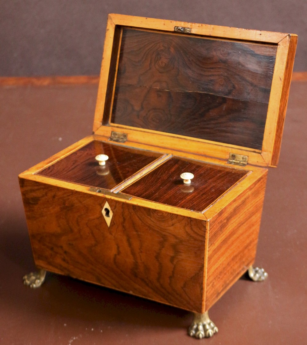 A Regency rosewood tapered oblong tea caddy featuring inlay stringing, a diamond bone escutcheon, and brass lion paw feet. View IV