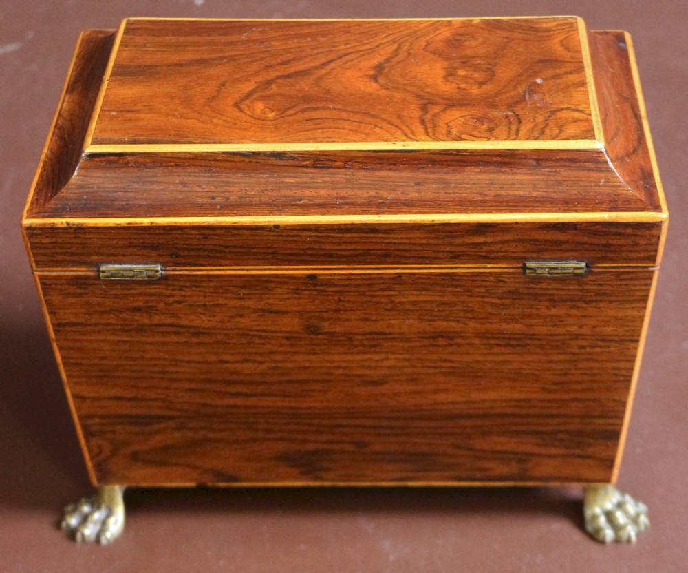 A Regency rosewood tapered oblong tea caddy featuring inlay stringing, a diamond bone escutcheon, and brass lion paw feet. View VI