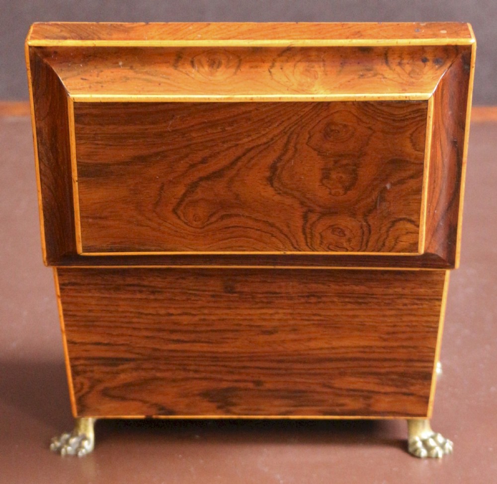 A Regency rosewood tapered oblong tea caddy featuring inlay stringing, a diamond bone escutcheon, and brass lion paw feet. View VII