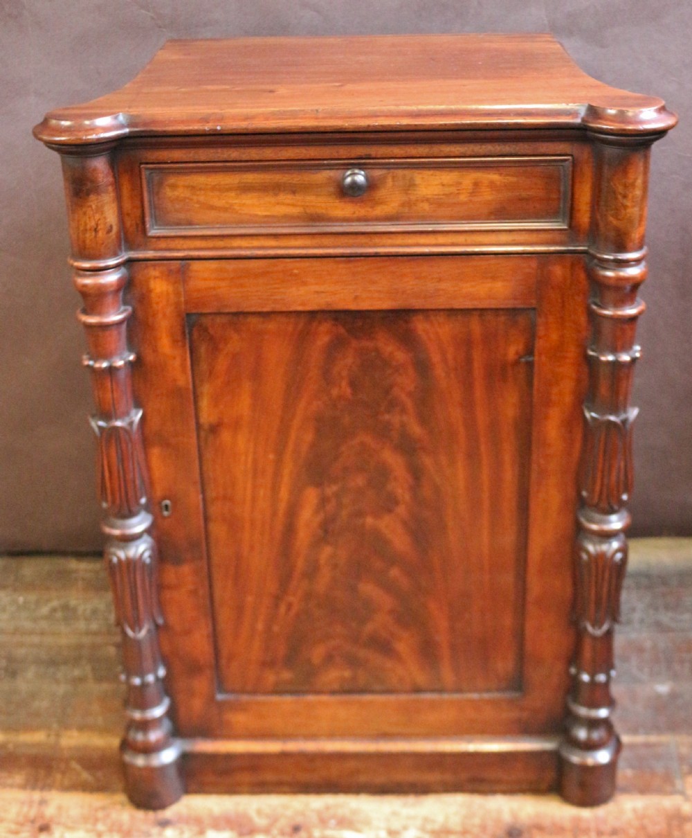 A William IV flame mahogany single-door bedside cupboard featuring a top drawer, carved acanthus leaf side columns, and a plinth base.