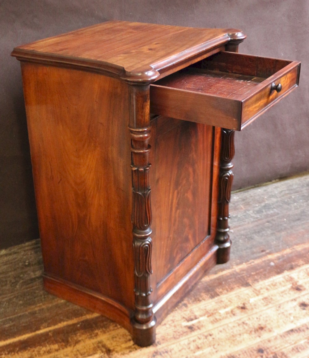 A William IV flame mahogany single-door bedside cupboard featuring a top drawer, carved acanthus leaf side columns, and a plinth base. View III