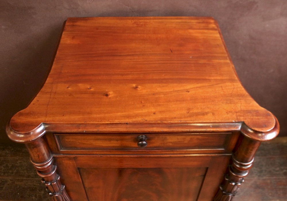 A William IV flame mahogany single-door bedside cupboard featuring a top drawer, carved acanthus leaf side columns, and a plinth base. View VII