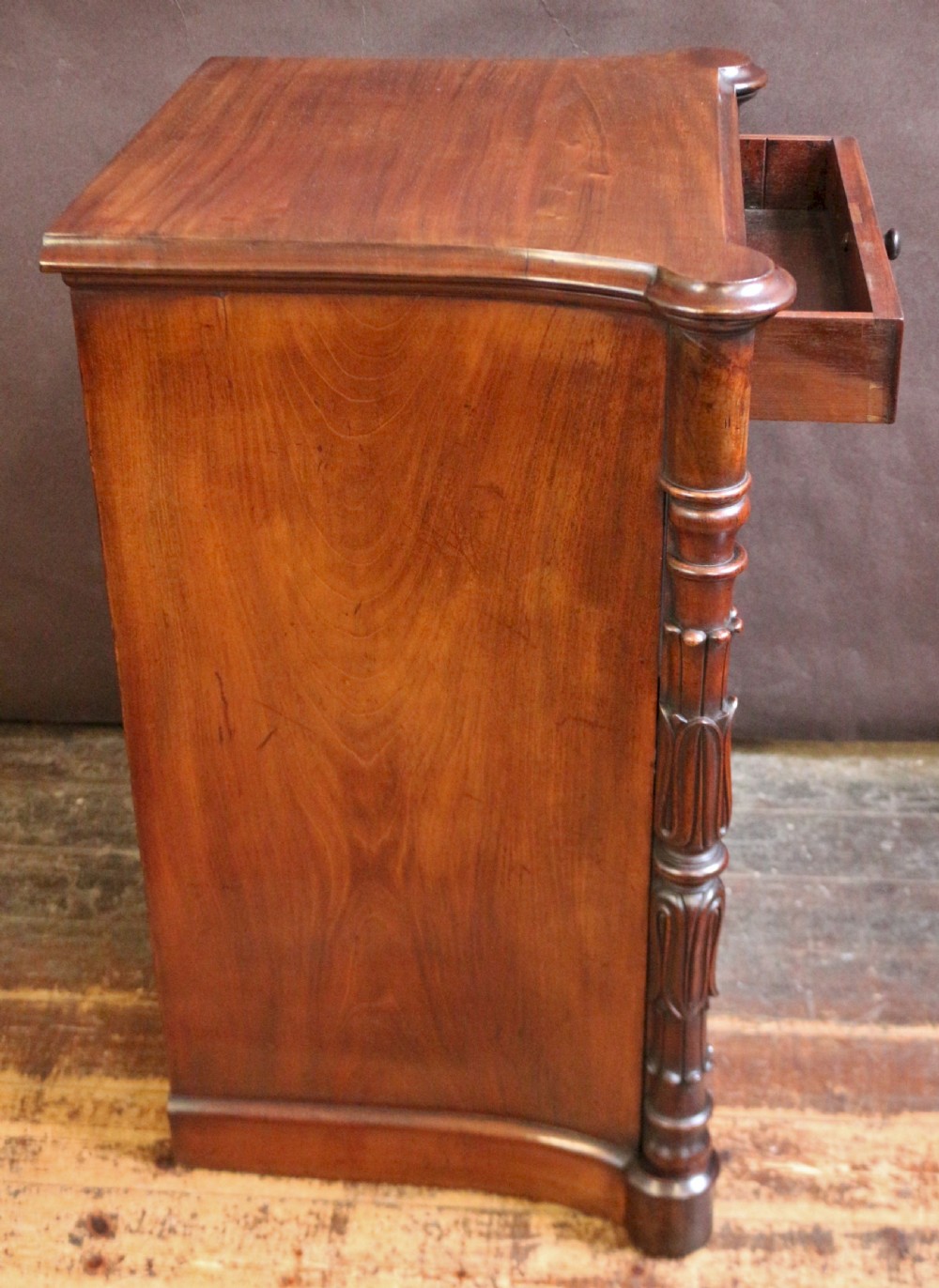 A William IV flame mahogany single-door bedside cupboard featuring a top drawer, carved acanthus leaf side columns, and a plinth base. View VIII