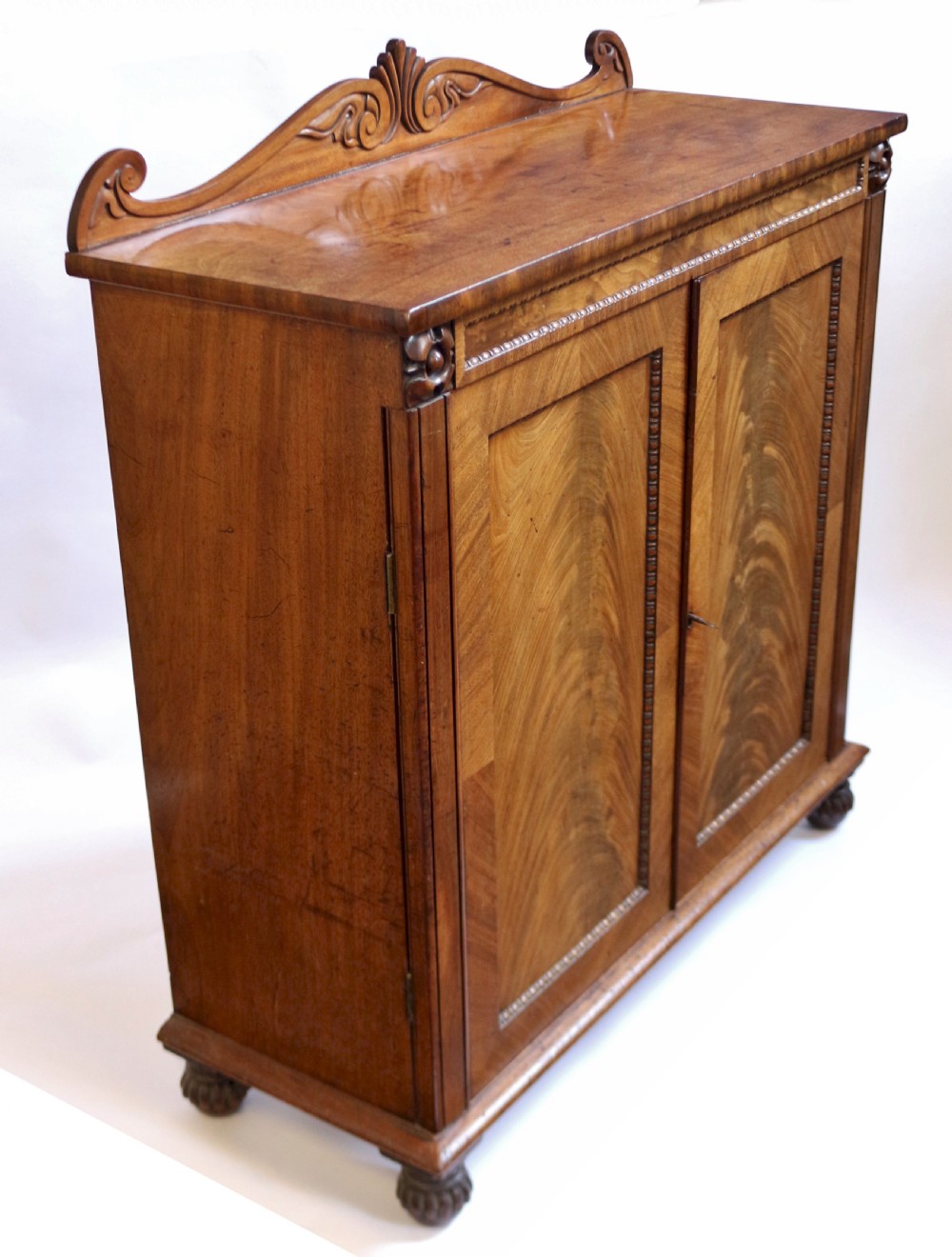 A William IV mahogany two-door side cupboard featuring flame mahogany door panels, a carved scroll backboard, and turned carved feet. View III