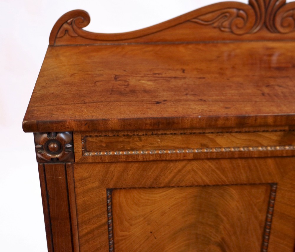 A William IV mahogany two-door side cupboard featuring flame mahogany door panels, a carved scroll backboard, and turned carved feet. View VI