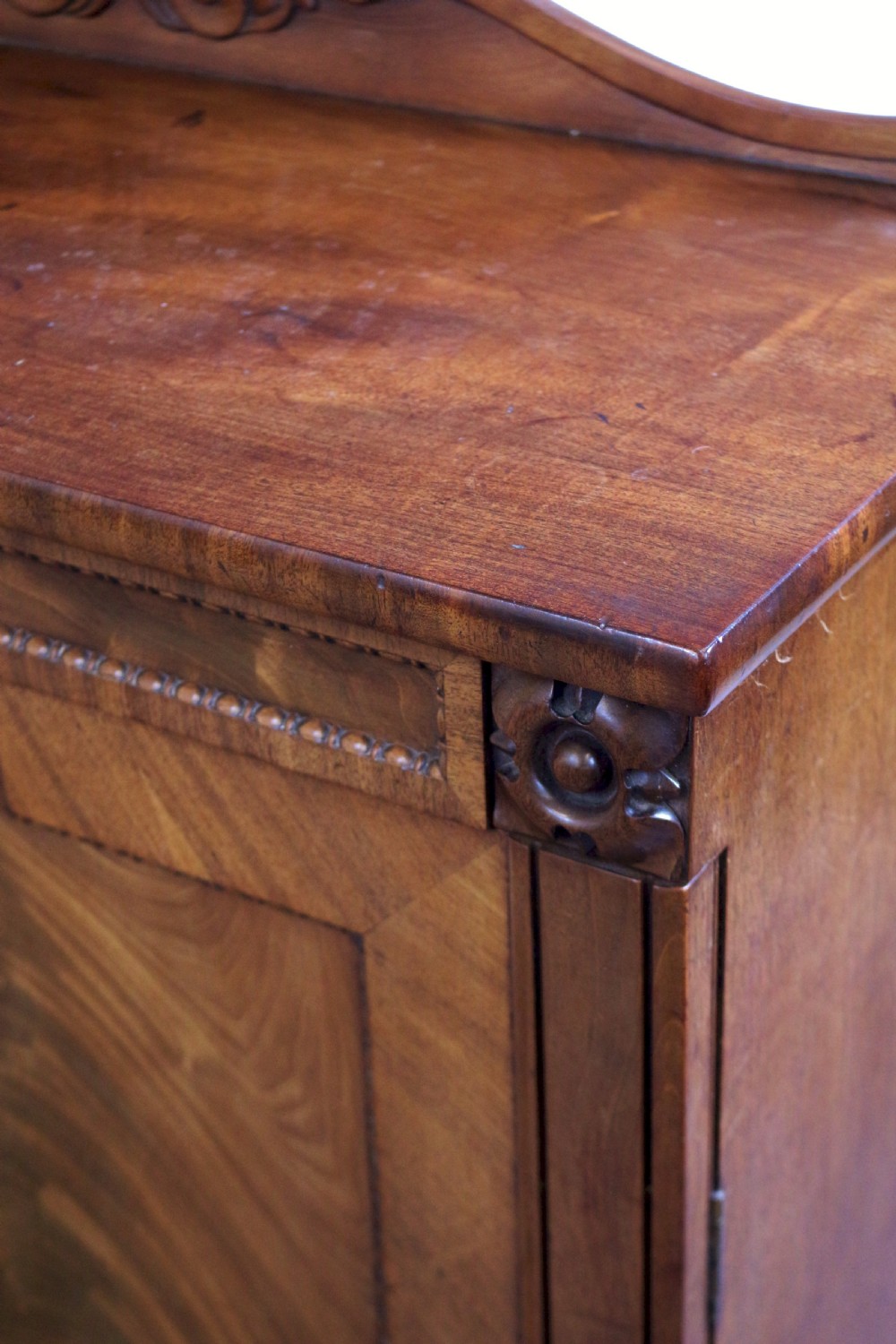 A William IV mahogany two-door side cupboard featuring flame mahogany door panels, a carved scroll backboard, and turned carved feet. View VIII