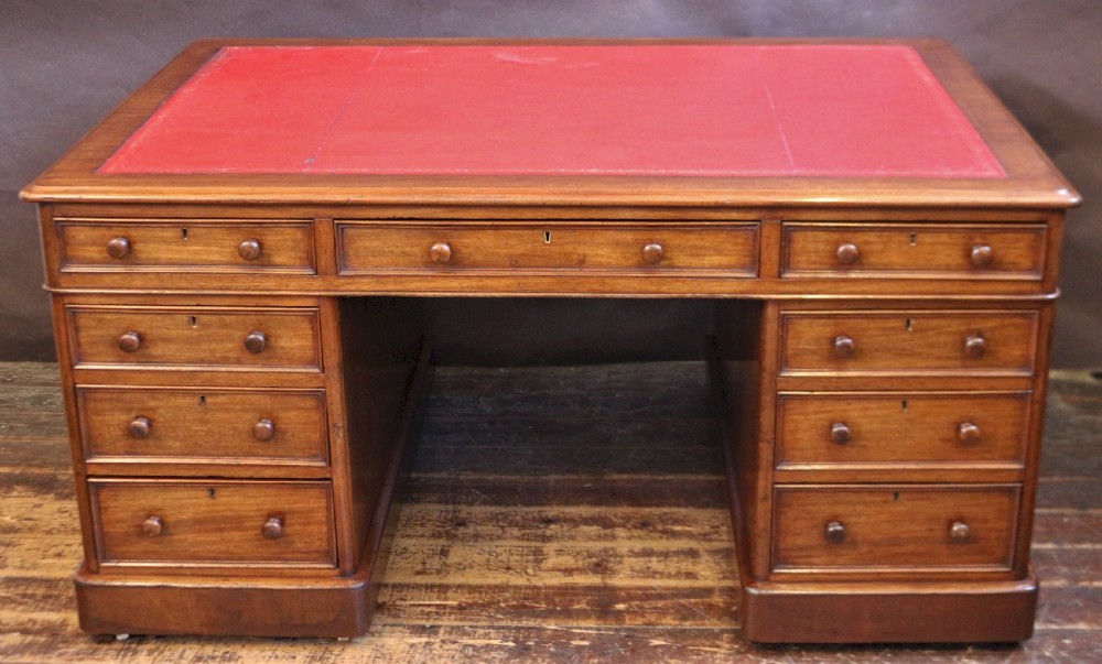 A Victorian mahogany three-part partners desk featuring a red leather writing inset and multiple drawers on two pedestals with turned wooden knobs.