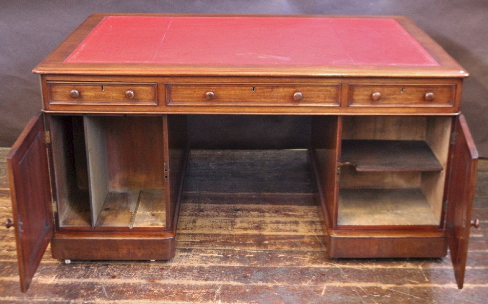 A Victorian mahogany three-part partners desk featuring a red leather writing inset and multiple drawers on two pedestals with turned wooden knobs. View V