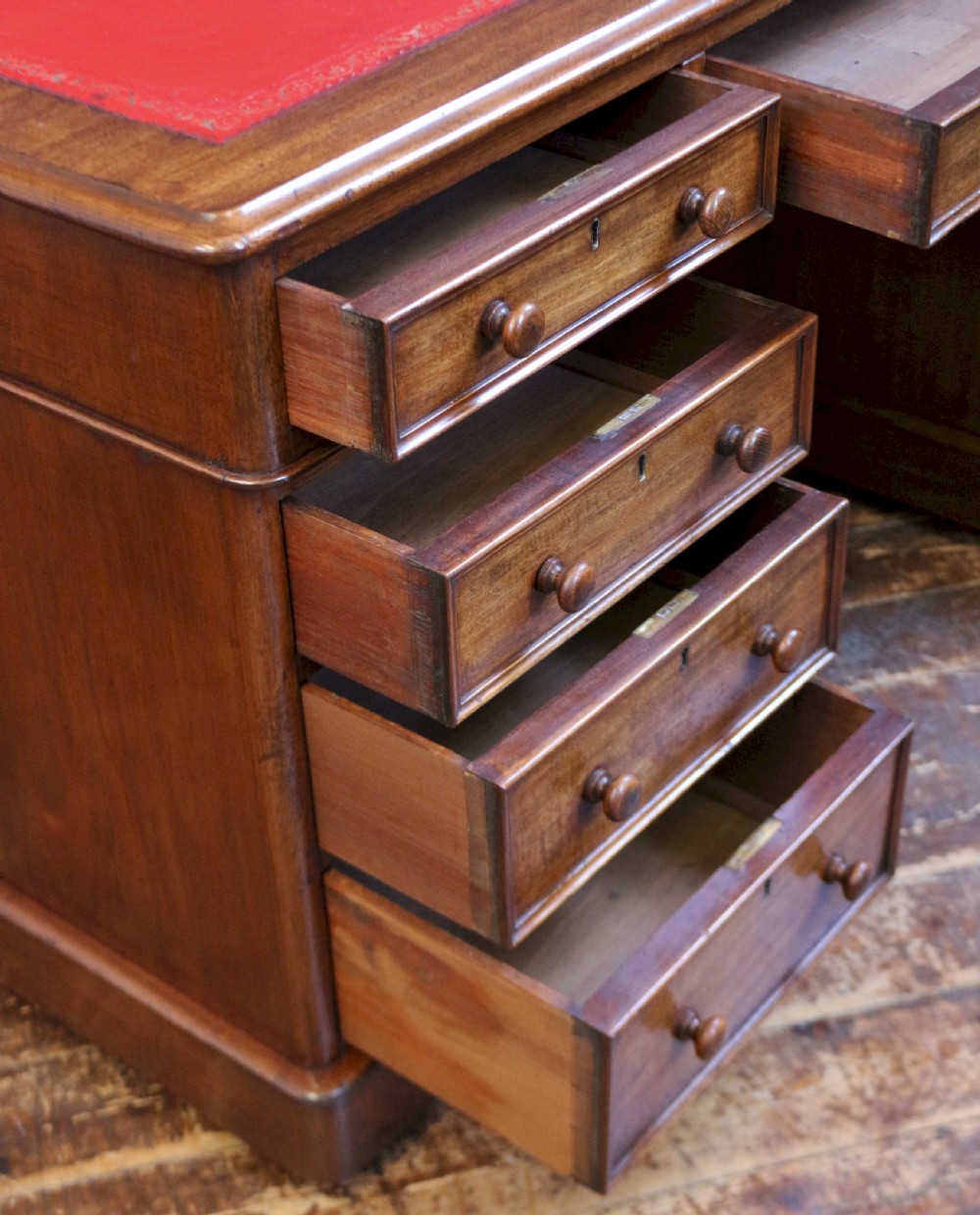 A Victorian mahogany three-part partners desk featuring a red leather writing inset and multiple drawers on two pedestals with turned wooden knobs. View VI