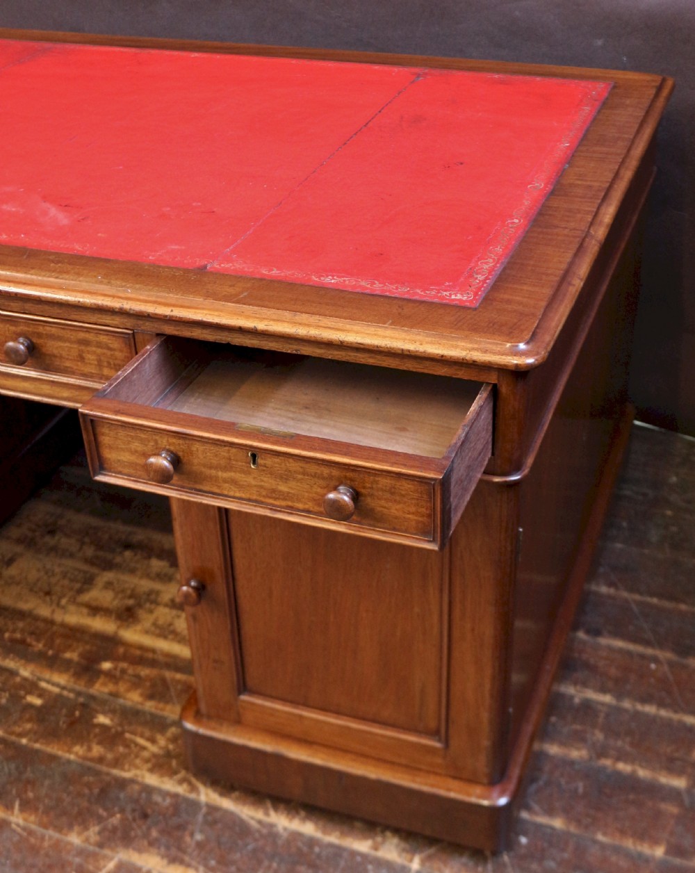 A Victorian mahogany three-part partners desk featuring a red leather writing inset and multiple drawers on two pedestals with turned wooden knobs. View VII
