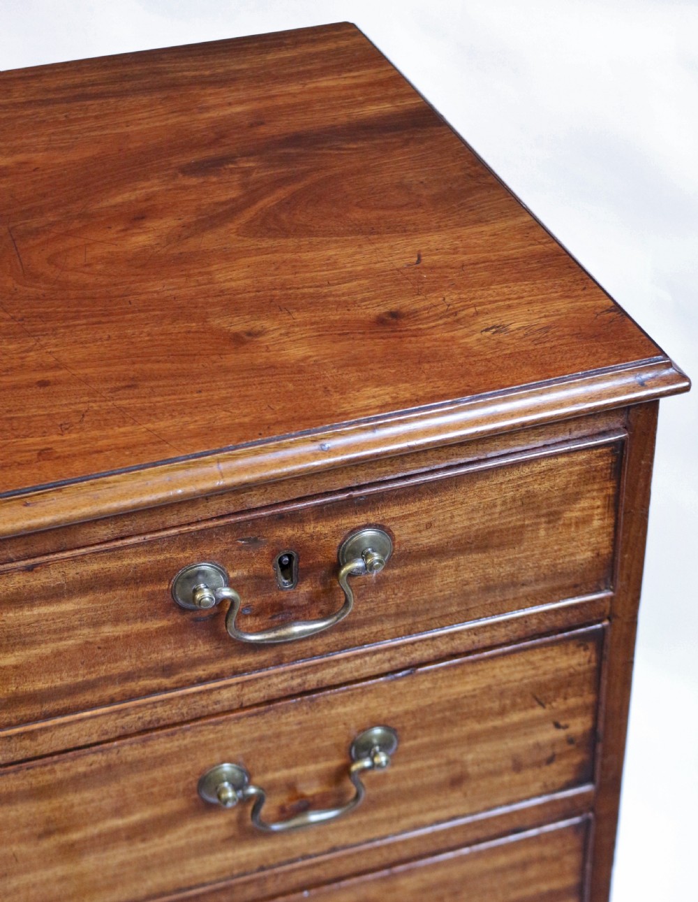 An antique Georgian mahogany chest of drawers featuring a two-over-three drawer configuration with brass swan-neck handles and shaped ogee bracket feet. View VII