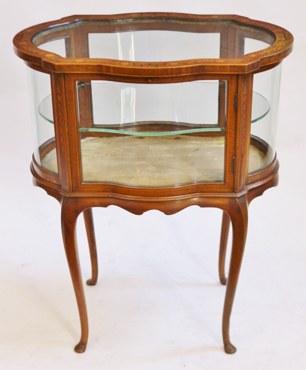 An Edwardian serpentine-shaped mahogany bijouterie cabinet featuring glass display panels, satinwood inlay along the top border, and slender cabriole legs.
