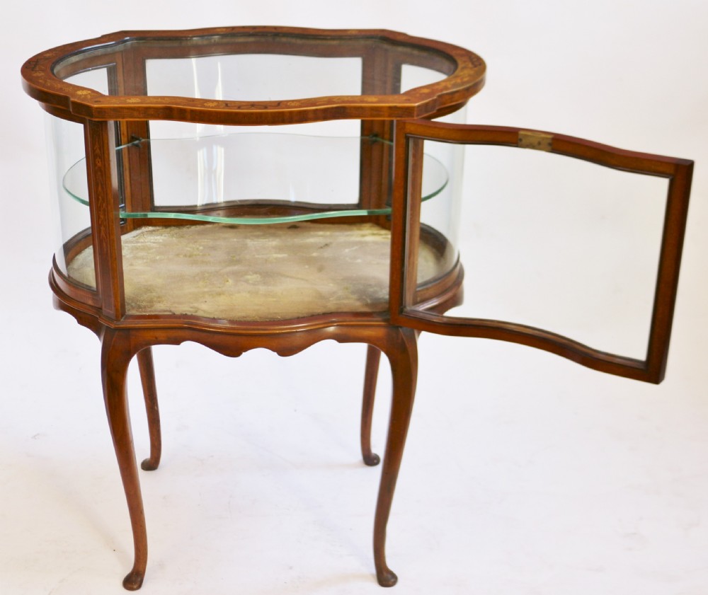 An Edwardian serpentine-shaped mahogany bijouterie cabinet featuring glass display panels, satinwood inlay along the top border, and slender cabriole legs. View II