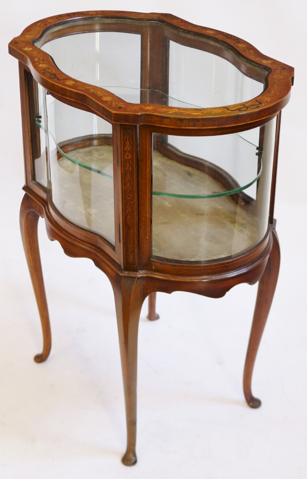 An Edwardian serpentine-shaped mahogany bijouterie cabinet featuring glass display panels, satinwood inlay along the top border, and slender cabriole legs. View IV