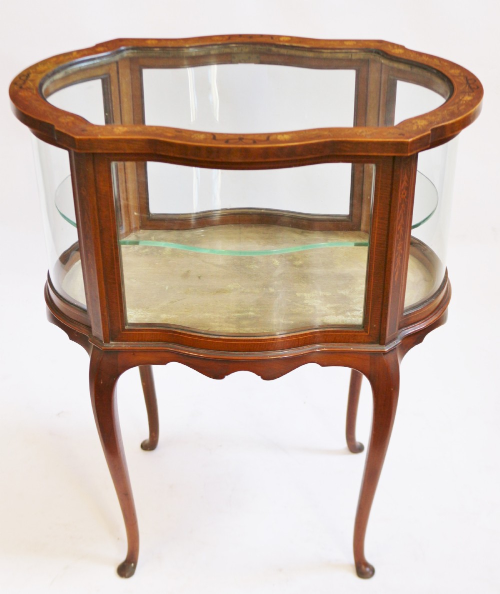 An Edwardian serpentine-shaped mahogany bijouterie cabinet featuring glass display panels, satinwood inlay along the top border, and slender cabriole legs. View V