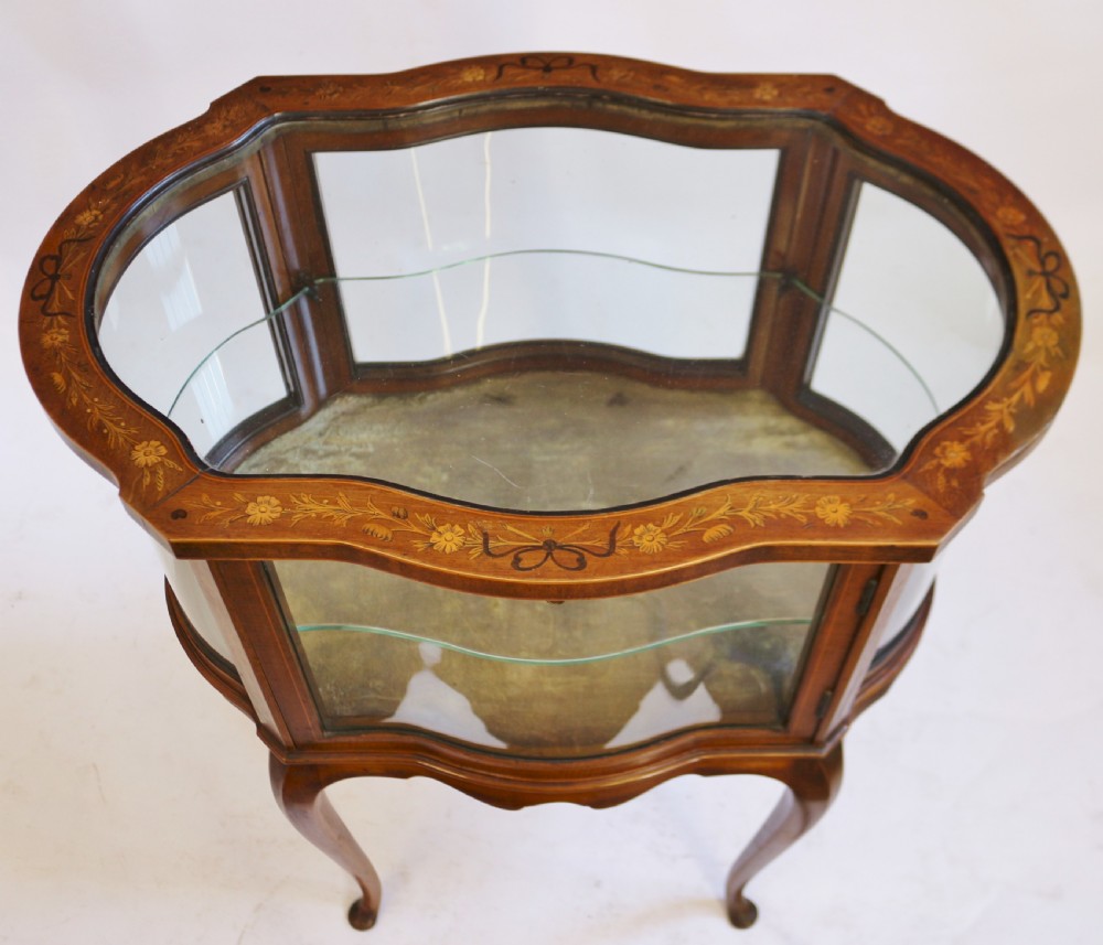 An Edwardian serpentine-shaped mahogany bijouterie cabinet featuring glass display panels, satinwood inlay along the top border, and slender cabriole legs. View VI