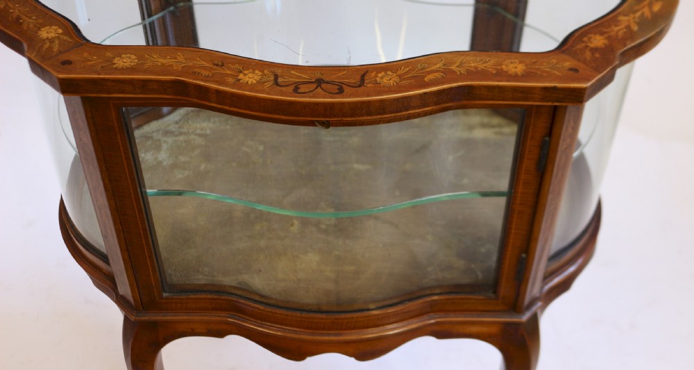 An Edwardian serpentine-shaped mahogany bijouterie cabinet featuring glass display panels, satinwood inlay along the top border, and slender cabriole legs. View VII