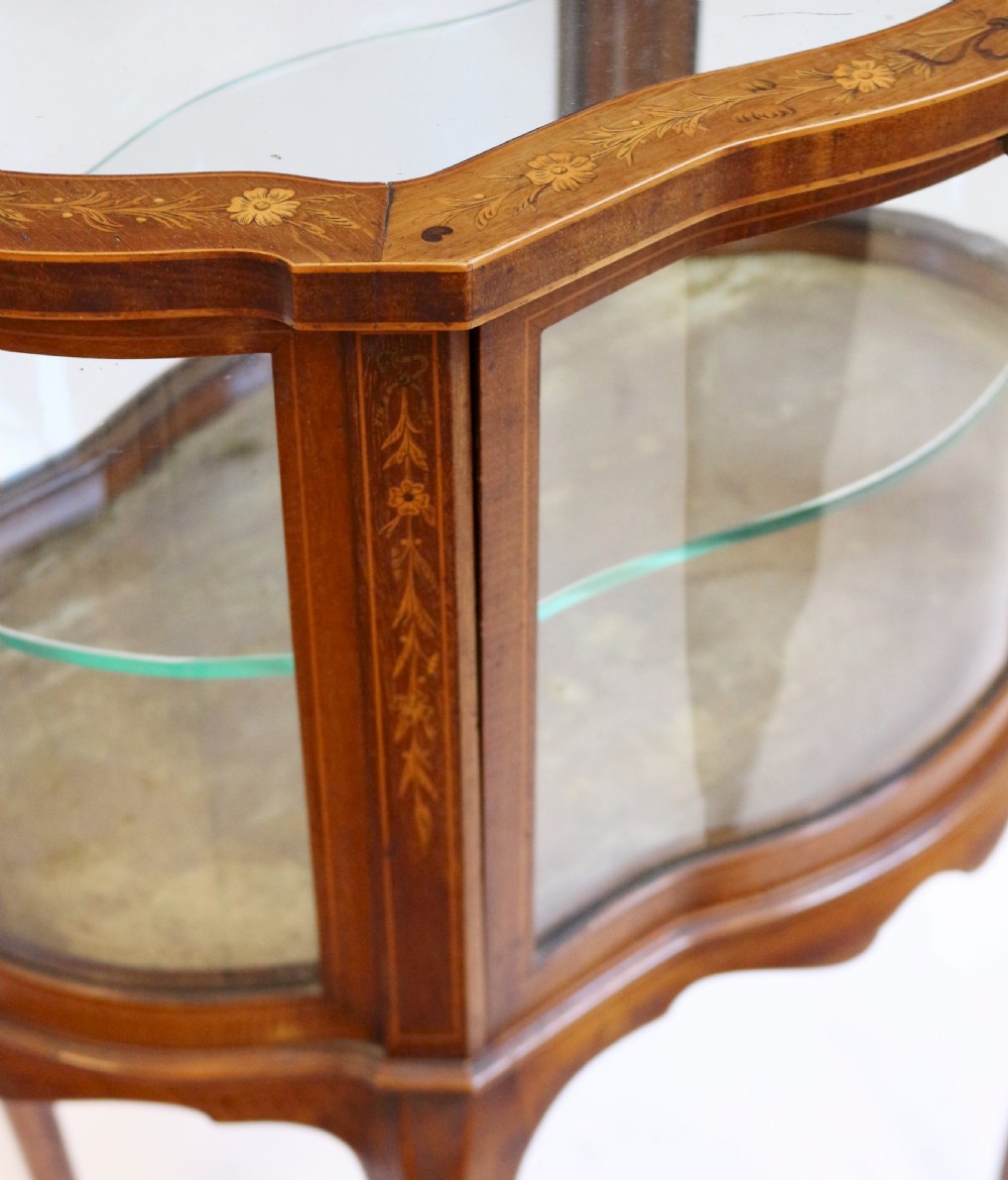 An Edwardian serpentine-shaped mahogany bijouterie cabinet featuring glass display panels, satinwood inlay along the top border, and slender cabriole legs. View VIII