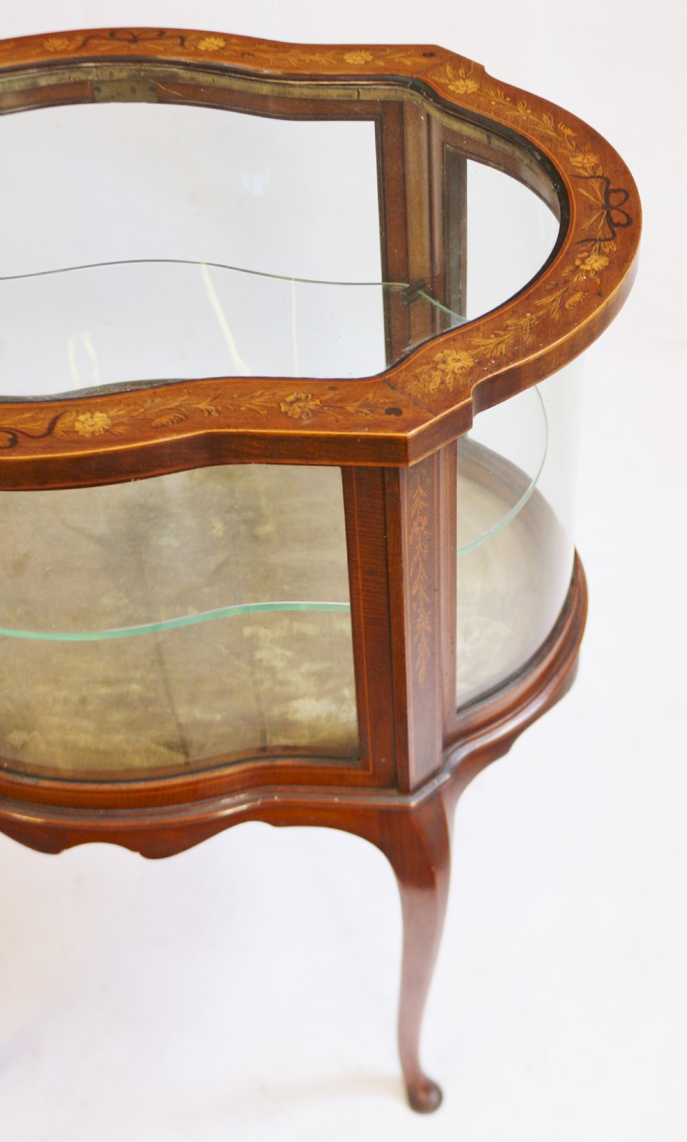 An Edwardian serpentine-shaped mahogany bijouterie cabinet featuring glass display panels, satinwood inlay along the top border, and slender cabriole legs. View IX