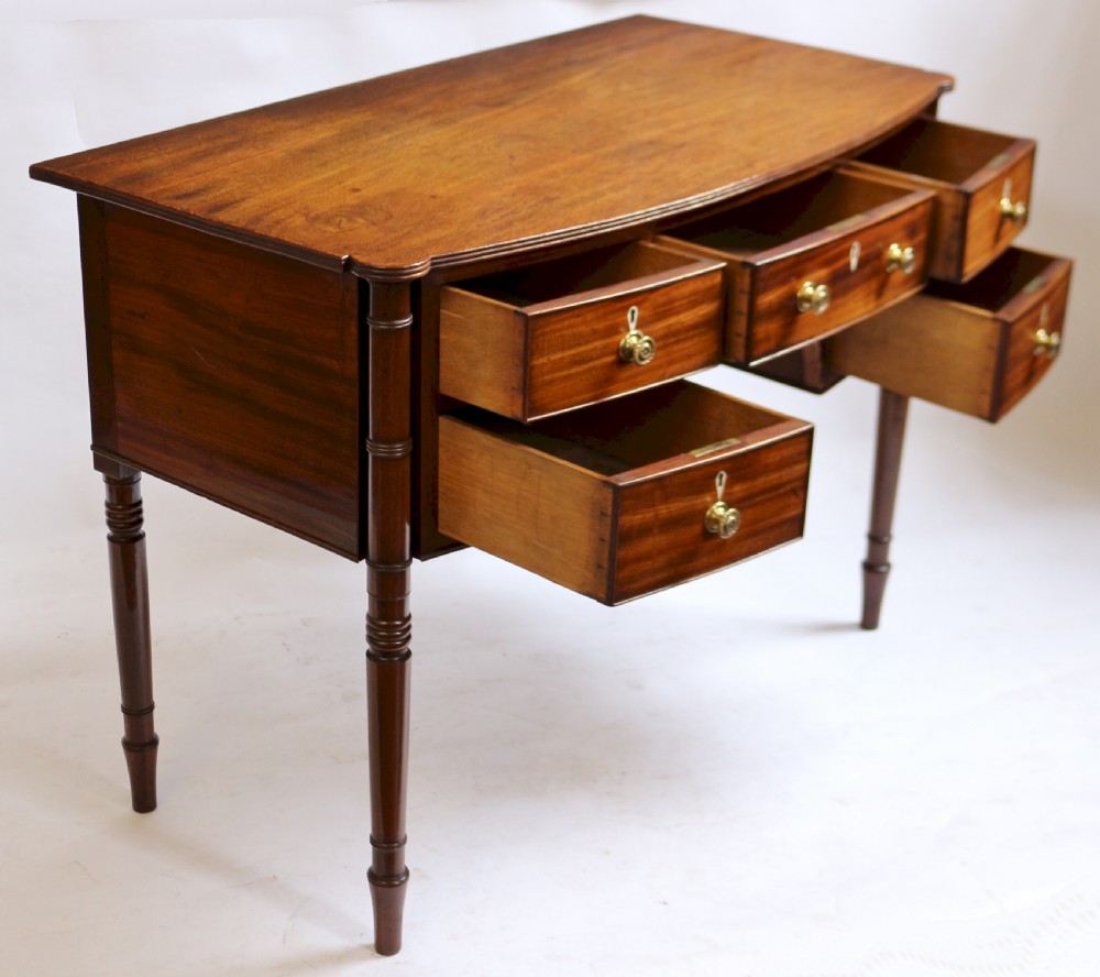 A George IV mahogany bowfront kneehole table with five drawers, brass knobs, teardrop escutcheons, and turned legs. View III