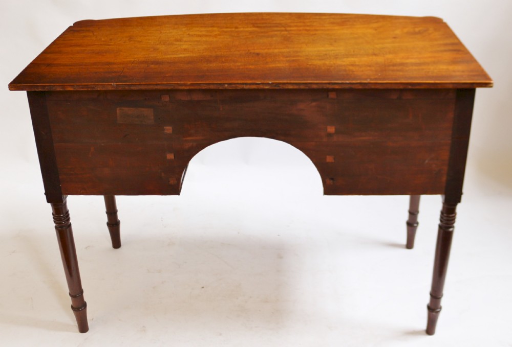 A George IV mahogany bowfront kneehole table with five drawers, brass knobs, teardrop escutcheons, and turned legs. View VI