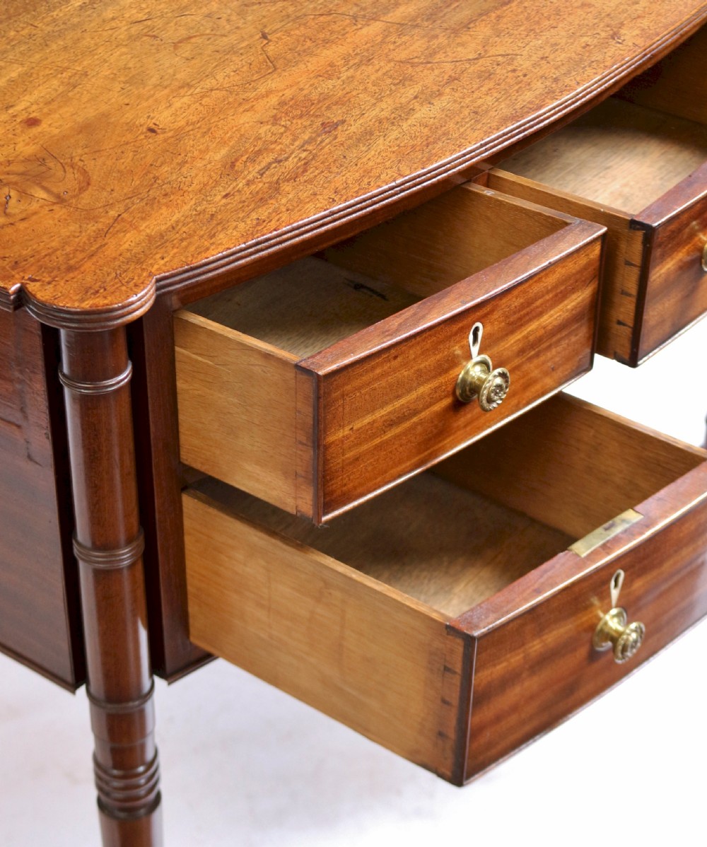 A George IV mahogany bowfront kneehole table with five drawers, brass knobs, teardrop escutcheons, and turned legs. View VII