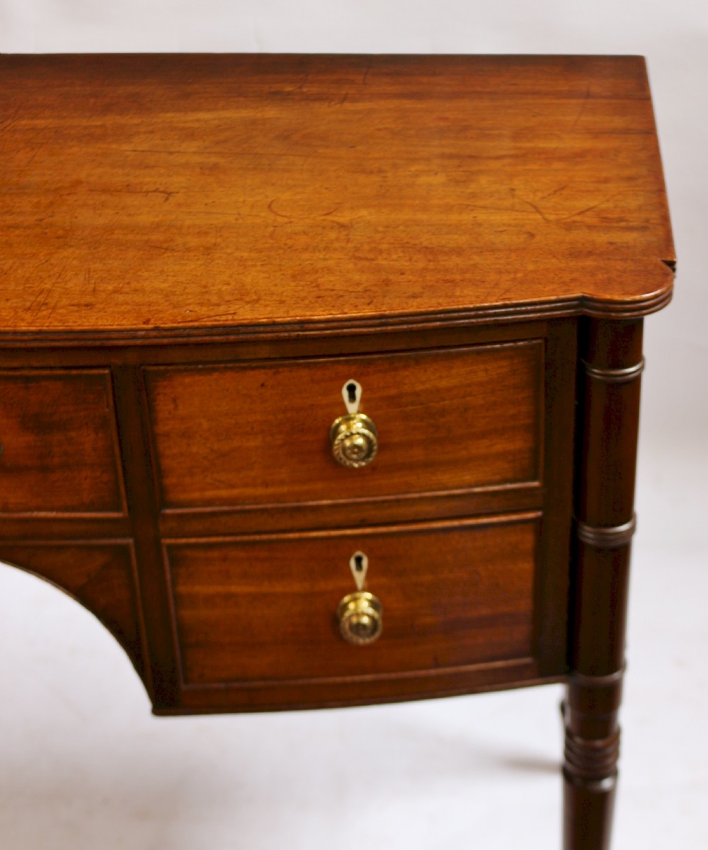 A George IV mahogany bowfront kneehole table with five drawers, brass knobs, teardrop escutcheons, and turned legs. View VIII