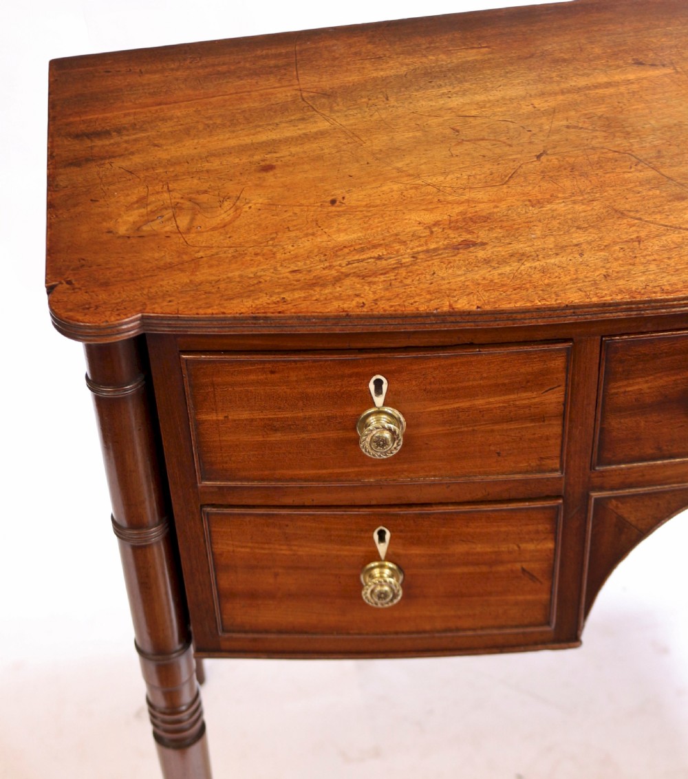 A George IV mahogany bowfront kneehole table with five drawers, brass knobs, teardrop escutcheons, and turned legs. View IX
