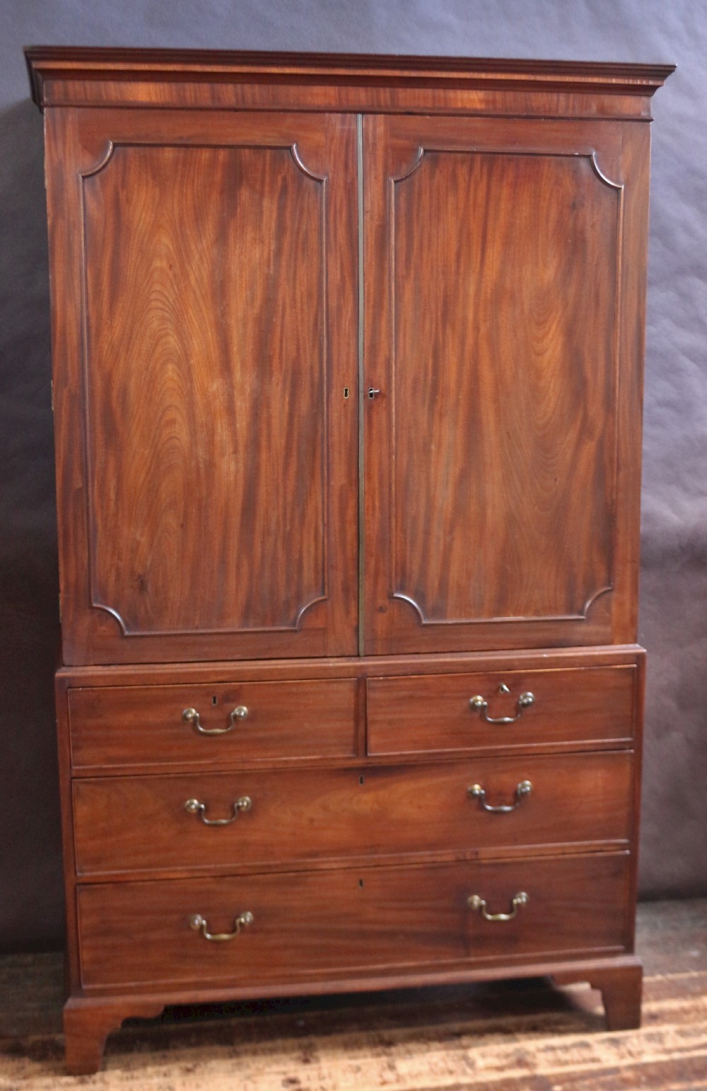 A Georgian mahogany linen press featuring panelled double doors above a chest with two short and two long drawers raised on bracket feet. View II